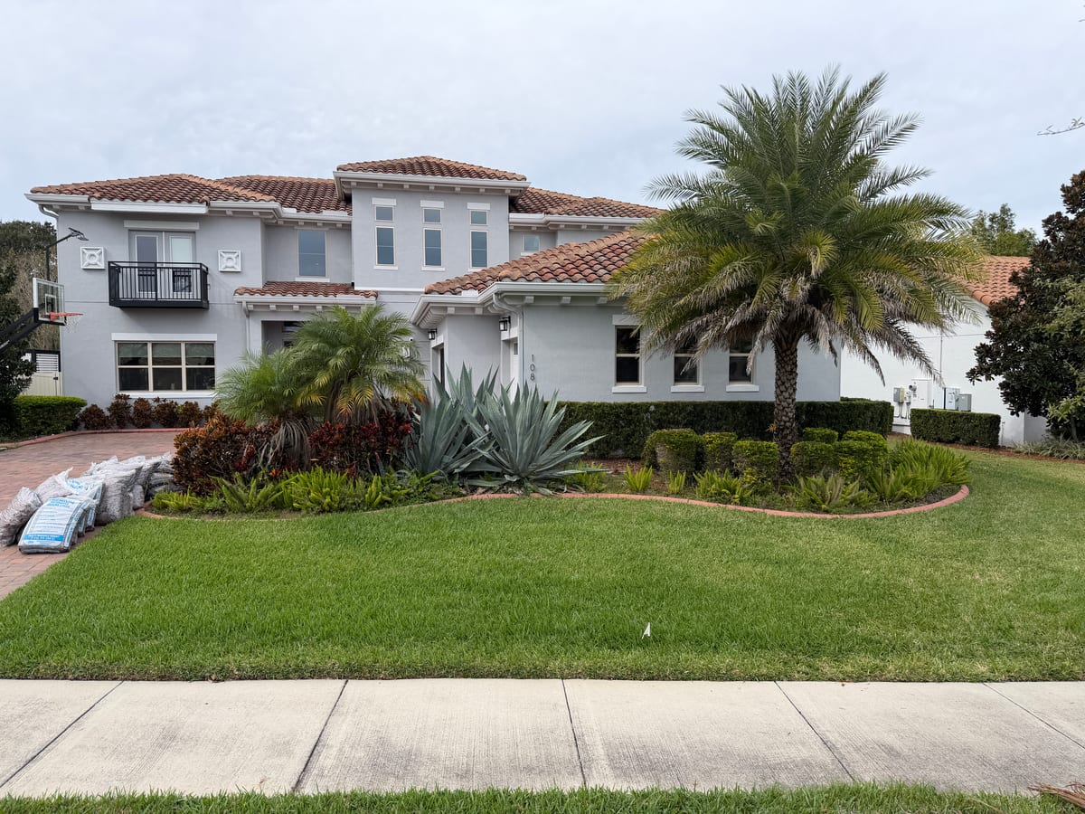 Two-story Florida home with manicured front lawn, tall palm, and tropical bedding